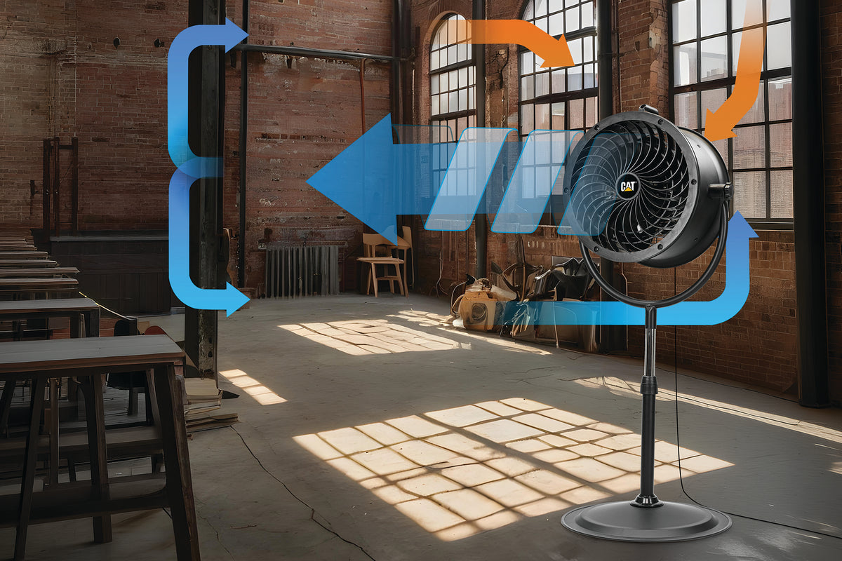 A black industrial fan on a stand in a sunlit brick warehouse, with blue and orange airflow arrows overlaid to illustrate circulation. The fan has a visible CF logo in the center.