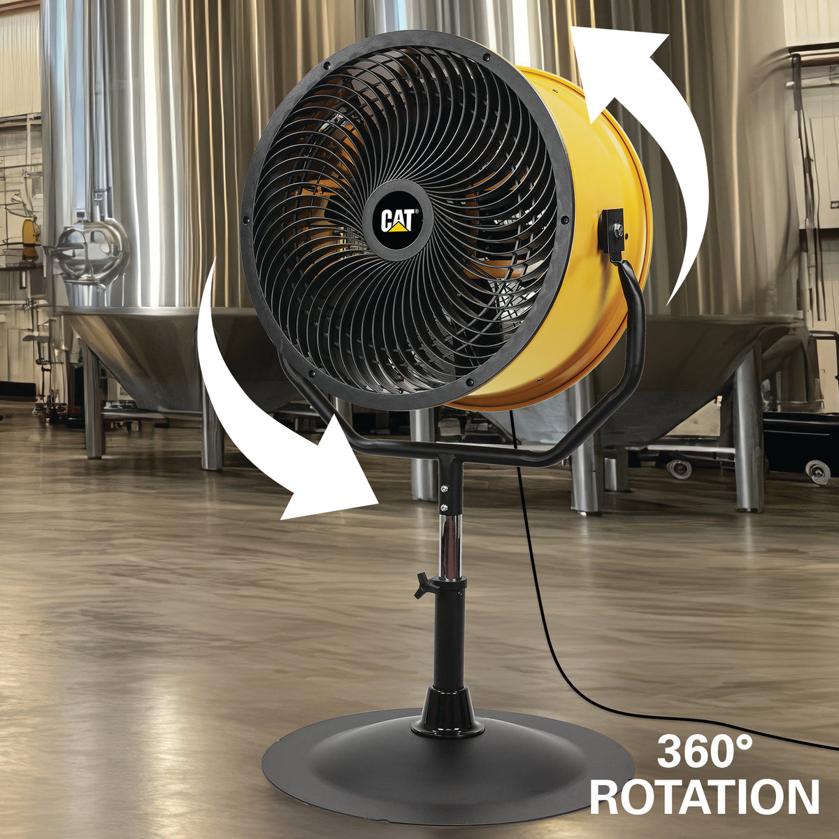 A CAT industrial fan with a black front grille and stand, yellow rear housing, and white arrows showing 360° rotation, set in an industrial brewery or processing facility with stainless steel tanks in the background.