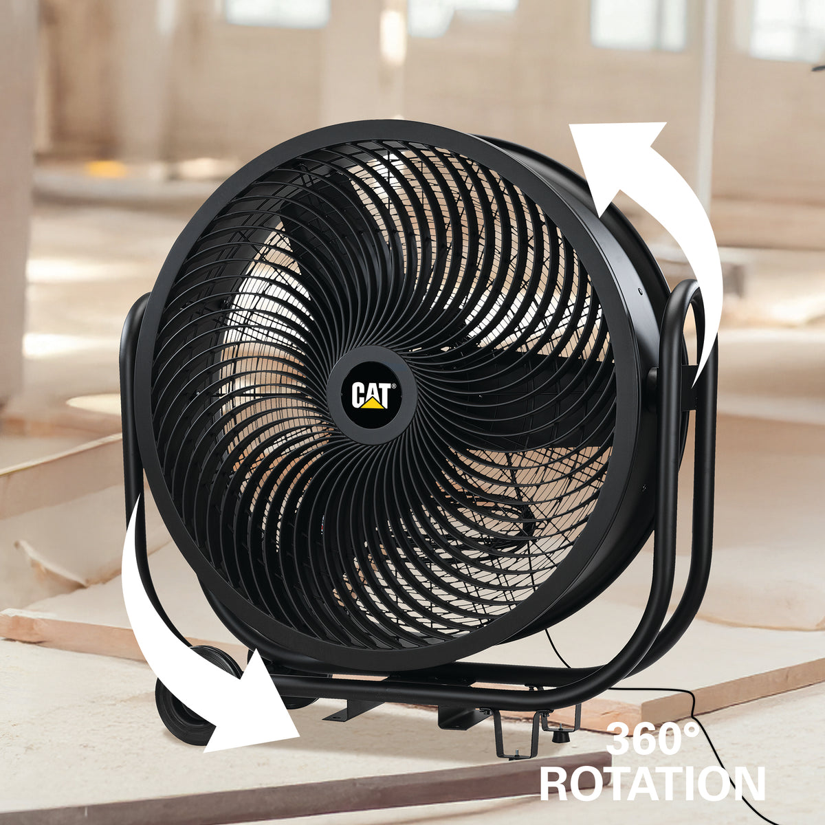 Black CAT industrial floor fan with white arrows showing 360° rotation, photographed in a real indoor setting with construction materials in the background.