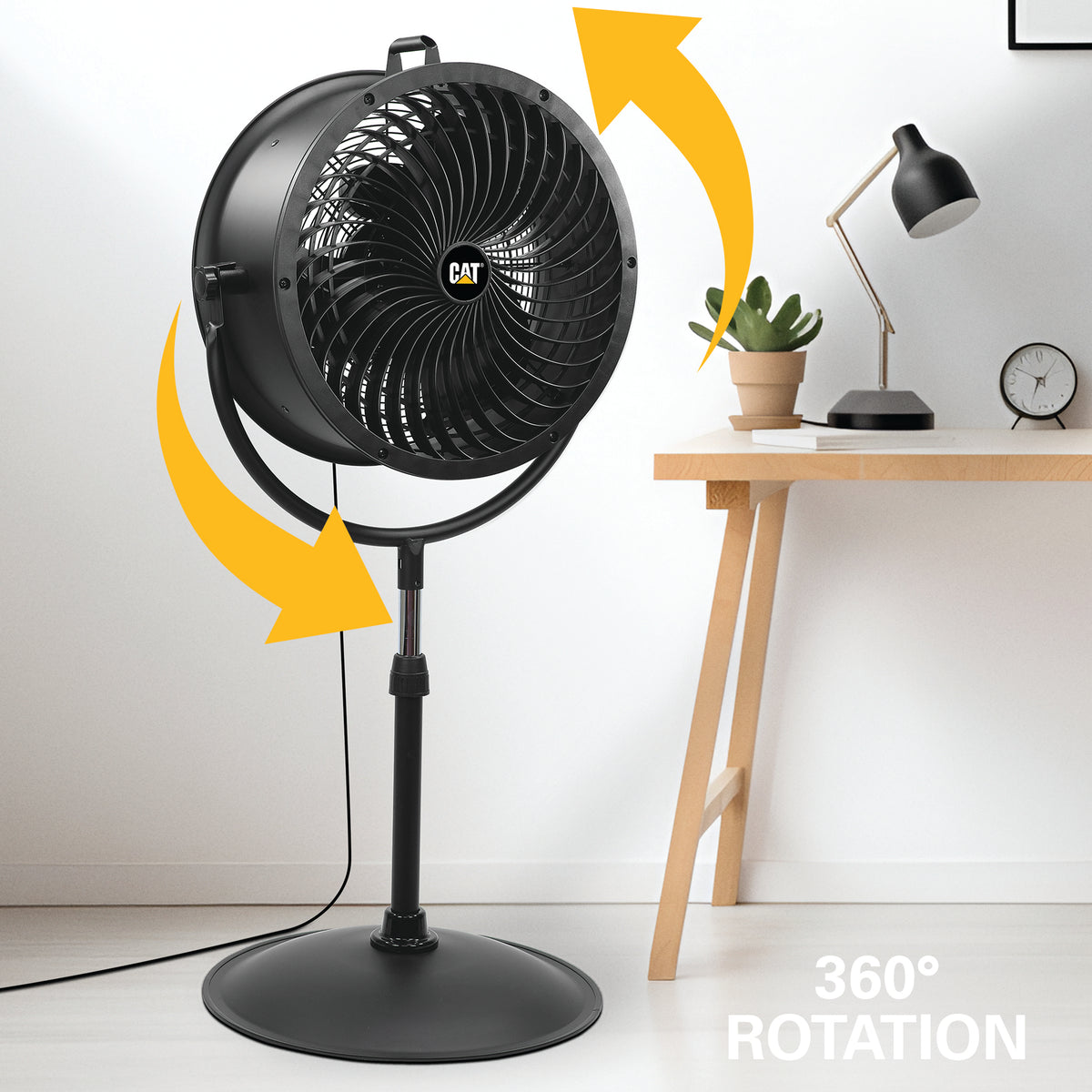 Black CAT pedestal fan with yellow arrows showing 360° rotation, set in a room next to a wooden desk with a lamp and plant.